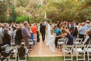 Wedding guests seated in white chairs during an outdoor ceremony with a floral arch and waterfall backdrop.