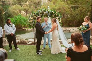 Wedding party gathering on landscaped grounds with trees and decorative lighting.