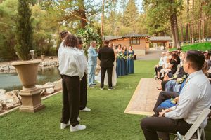 Wedding guests seated in rows of chairs on a lawn in front of a rustic cabin venue.