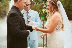 An intimate wedding ceremony moment under a floral arch with a flowing white gown and formal attire.
