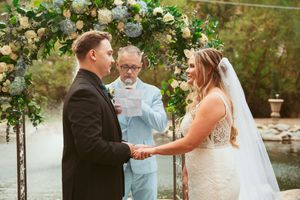 Wedding ceremony taking place under an elegant floral arch with white and green blooms.