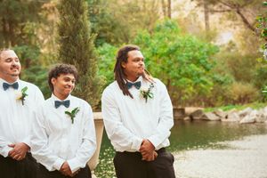 Wedding party in formal attire posed by a pond wearing black bowties and white dress shirts.