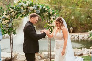 An emotional exchange during wedding ceremony beneath an ornate floral arch.
