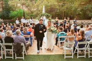 Wedding ceremony processional on green lawn with white chairs and guests watching the couple walk down the aisle.