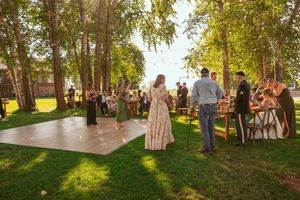 Guests gather on an outdoor dance floor surrounded by trees during a sunny afternoon reception.
