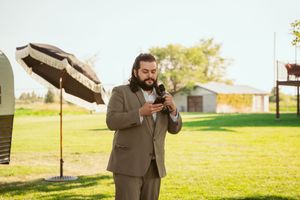 A person in a suit checks their phone during an outdoor event on a sunny day.