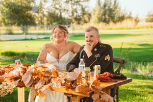 Long wooden tables set for an outdoor wedding reception with fall-colored decor and floral arrangements.