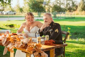 Newlyweds share a meal at an outdoor reception table decorated with autumn-colored linens.