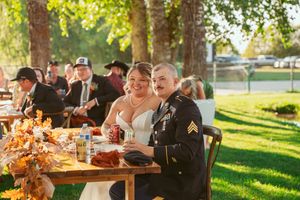 Military service member and companion celebrate at an outdoor wedding reception table during golden hour.