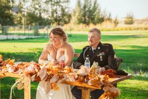 Couple enjoying their wedding meal at rustic outdoor table decorated with autumn-themed arrangements.