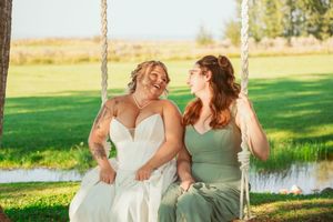 Two people sharing a joyful moment while sitting together on a wooden swing in a sunlit garden.