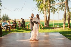 Outdoor wedding venue decorated with hanging string lights and surrounded by green trees at sunset.
