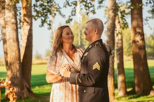 Military service member and companion share an intimate moment among birch trees in warm sunlight.