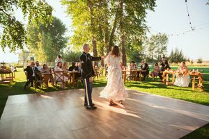 Wedding guests gathered outdoors at sunset around wooden benches for a rustic celebration.