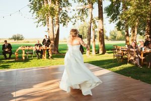 Dancing on an outdoor wooden deck at golden hour during a garden wedding celebration, with trees and string lights overhead.