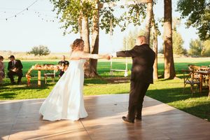 A couple shares their first dance on an outdoor wooden dance floor during a sunny daytime wedding celebration.