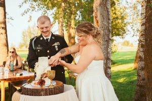 A couple cuts their rustic wedding cake together on a wooden stand outdoors.