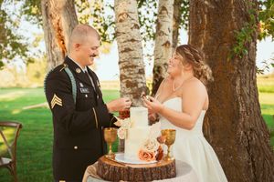 A couple shares a moment while cutting their wedding cake on a rustic wood stand outdoors.