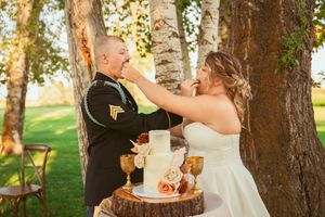 A couple shares a playful cake-feeding moment at their rustic outdoor wedding.
