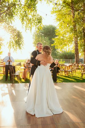 A couple shares their first dance on an outdoor dance floor at sunset with yellow autumn trees and guests in the background.