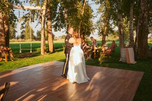 Couple sharing first dance on outdoor wooden dance floor surrounded by trees and guests.