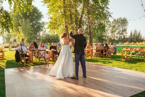 A couple dances on a wooden deck at their outdoor wedding reception under trees.