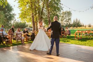 Couple dancing on wooden platform at outdoor wedding reception with string lights and garden setting.