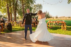 A couple shares their first dance on an outdoor wooden dance floor at a rustic wedding venue during golden hour.