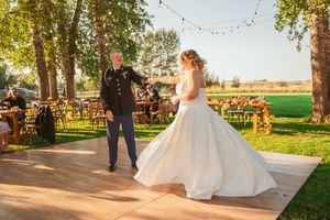 A couple shares their first dance on an outdoor dance floor at a rustic countryside wedding reception with string lights overhead.