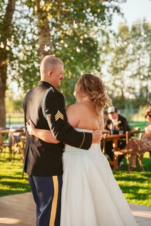 Military servicemember and bride share romantic dance moves in a sunlit outdoor wedding celebration at sunset.