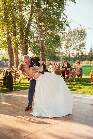 A couple shares a romantic dip while dancing on an outdoor patio filled with trees and string lights at sunset.