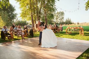 A couple shares an intimate dance on a wooden platform during their outdoor garden wedding reception.