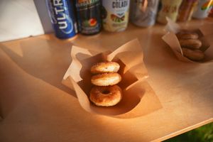 Mini slider sandwiches served in brown paper wrapper with various beverages in background.