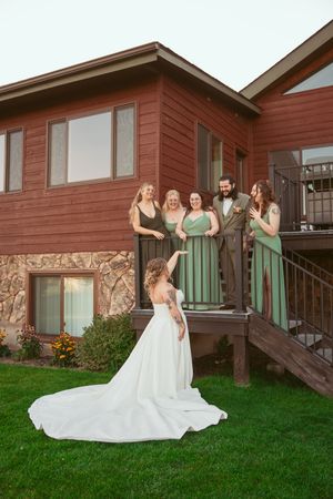 A sequence of five joyful wedding party photos showing bridesmaids in sage green dresses and a bride in white on a lawn.