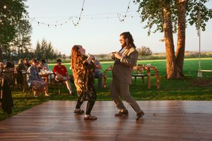 Two dancers swing dancing on a wooden deck with festive string lights and trees at golden hour.