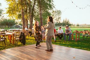 A rustic outdoor wedding reception venue set up under trees with wooden chairs at sunset.