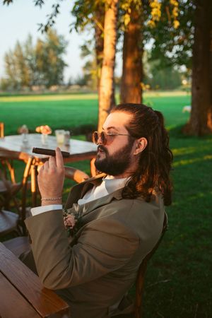 Four sequential photos showing a person smoking a cigar while sitting outdoors at sunset in a brown jacket.