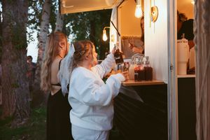 Guests in white sweaters ordering drinks from an illuminated outdoor bar at dusk.