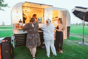 Vintage airstream food trailer illuminated at dusk with customers standing outside on a grassy lawn.
