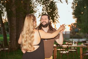 A couple dances together outdoors at sunset with twinkle lights and trees in the background.