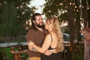 A couple shares an intimate embrace during sunset at an outdoor wedding reception.