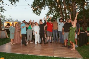 A group of people celebrating outdoors on a wooden deck at dusk with an RV visible in the background.