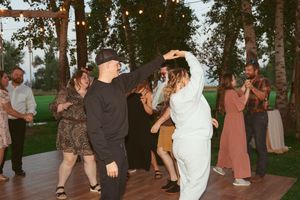 Wedding guests dance together on a grassy lawn during an outdoor evening reception.
