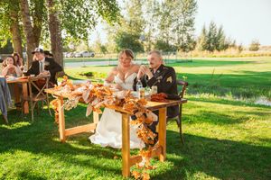 Elegant outdoor autumn reception setup with wooden benches and warm lighting at golden hour in a grassy field.