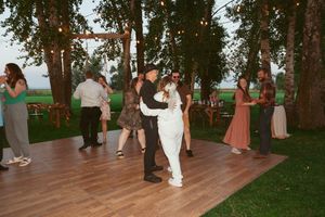 Couples dancing on an outdoor wooden deck surrounded by tall trees during a wedding reception.