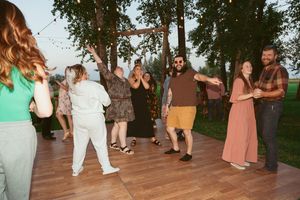 Wedding guests dance together on a rustic wooden deck during an outdoor celebration at sunset.