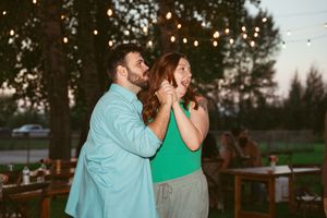Couples sway to music under twinkling string lights at an outdoor evening reception.