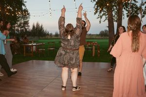 People dancing together on a wooden deck at an outdoor celebration with peach-colored sunset lighting.