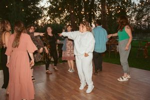 People dancing and celebrating at a festive outdoor reception with wooden floors at sunset.
