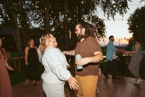 People dancing together at an outdoor evening party with trees in the background and warm lighting.